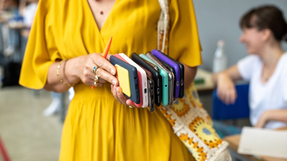 teacher holding stack of cell phones